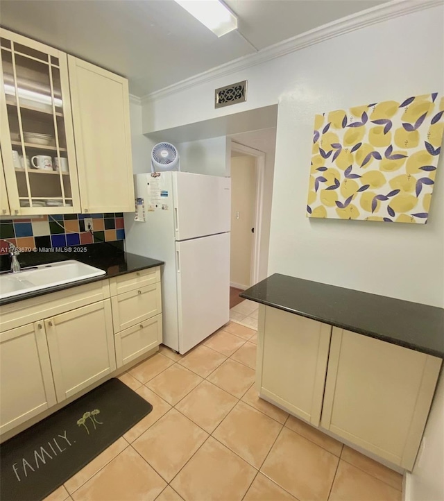 kitchen with light tile patterned floors, freestanding refrigerator, a sink, crown molding, and backsplash