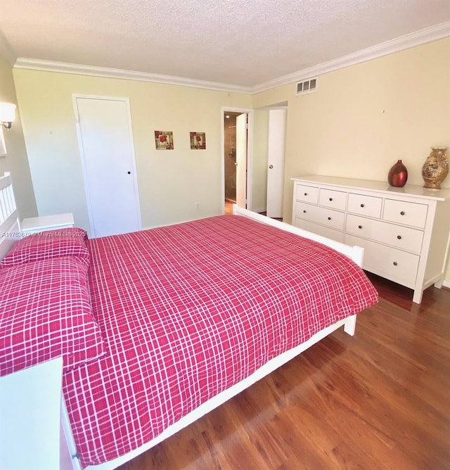 bedroom featuring a textured ceiling, wood finished floors, visible vents, and ornamental molding