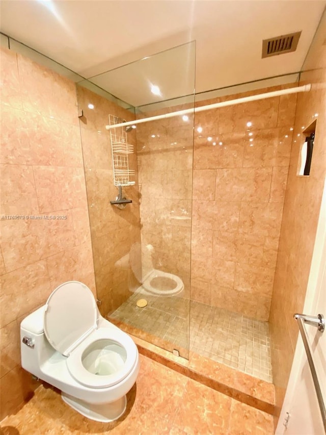 bathroom with visible vents, toilet, tiled shower, and tile walls