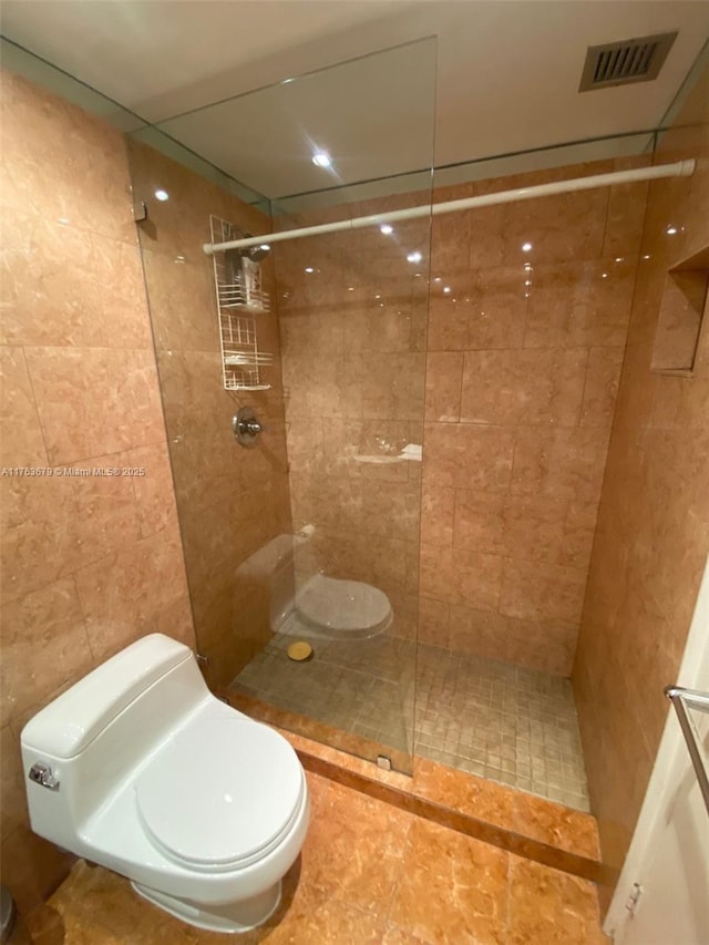 bathroom featuring toilet, a tile shower, tile walls, and visible vents