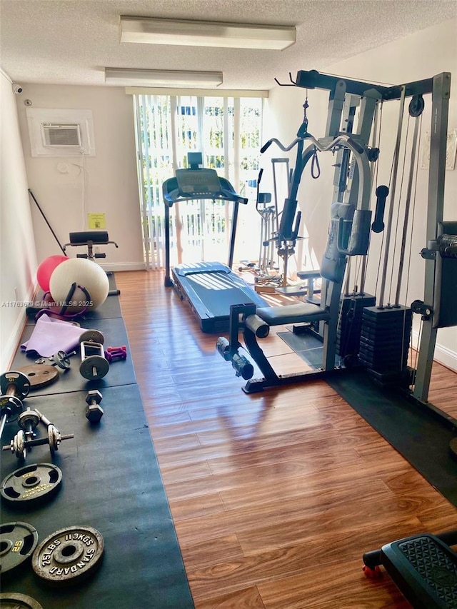 workout room featuring a textured ceiling, wood finished floors, an AC wall unit, and baseboards