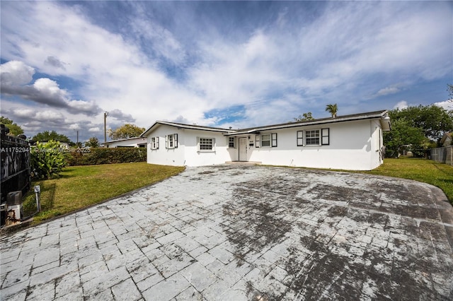 rear view of house featuring decorative driveway, a lawn, and stucco siding