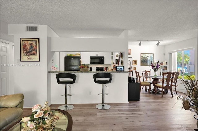 kitchen featuring visible vents, black appliances, a kitchen breakfast bar, wood finished floors, and white cabinetry