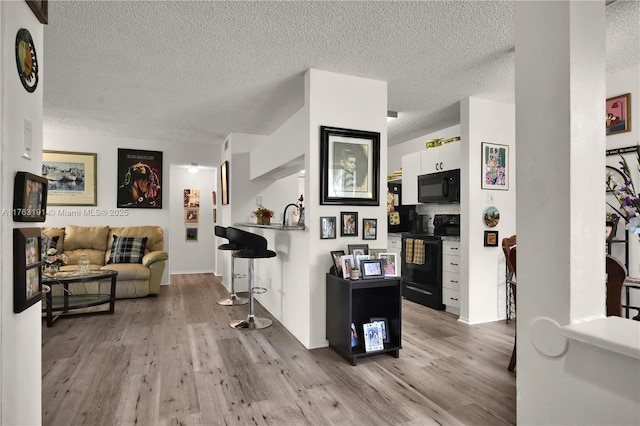 living area featuring baseboards, light wood-type flooring, and a textured ceiling