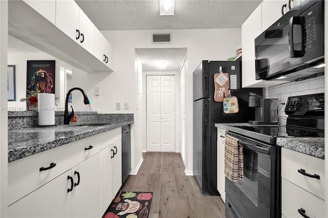 kitchen featuring light wood-type flooring, visible vents, black appliances, a sink, and a textured ceiling