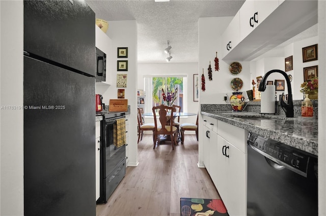 kitchen with black appliances, light wood-style flooring, a sink, dark countertops, and a textured ceiling