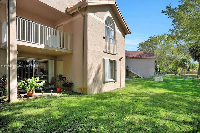 back of house featuring stucco siding, a lawn, stairs, and a balcony