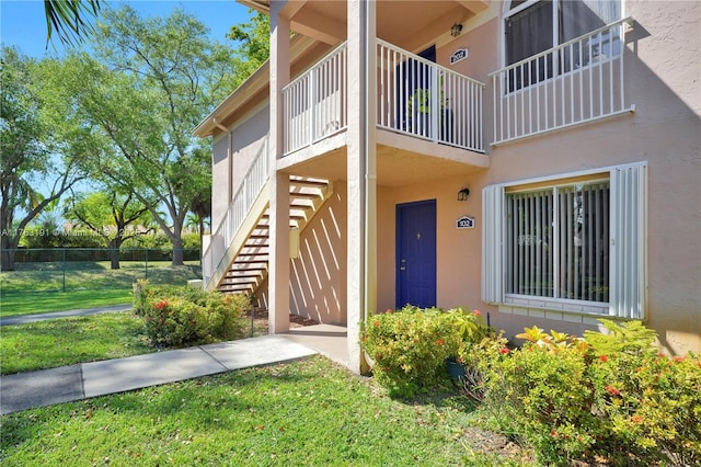 view of exterior entry featuring fence, a lawn, and stucco siding