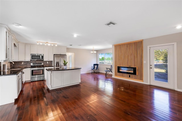 kitchen featuring dark countertops, a center island, decorative backsplash, stainless steel appliances, and a sink