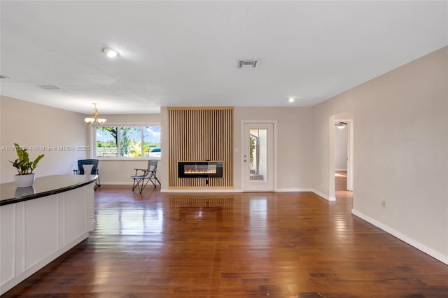 unfurnished living room with visible vents, baseboards, a chandelier, wood finished floors, and a glass covered fireplace