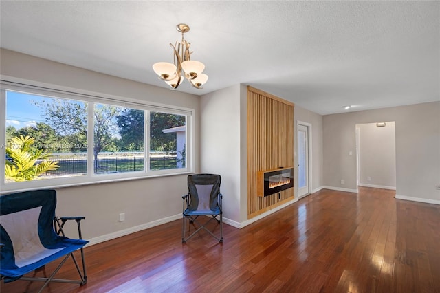 living area featuring a large fireplace, baseboards, a chandelier, and hardwood / wood-style flooring