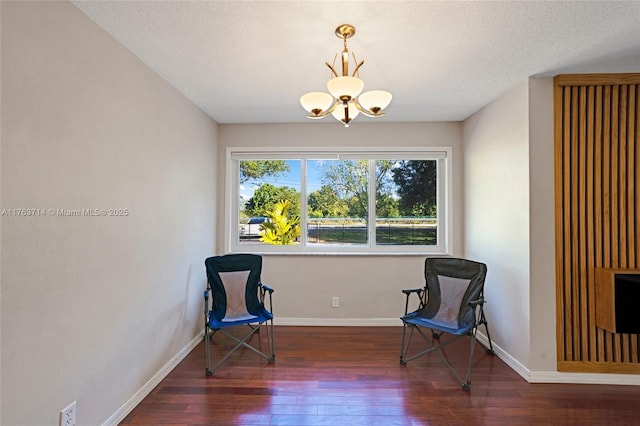 living area featuring an inviting chandelier, wood finished floors, baseboards, and a textured ceiling