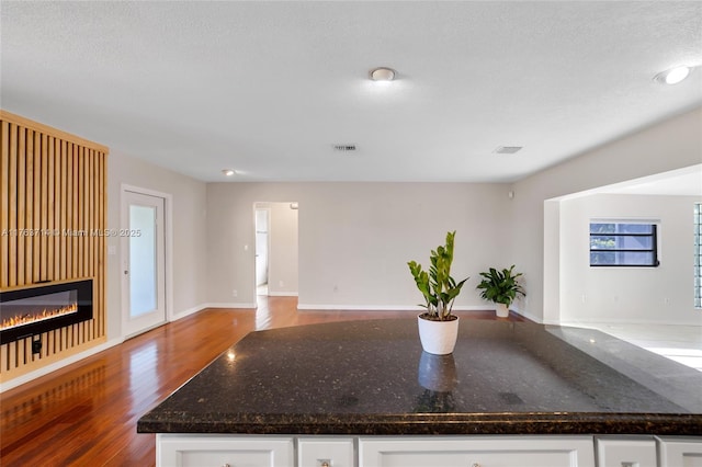 kitchen with open floor plan, white cabinetry, a glass covered fireplace, and wood finished floors