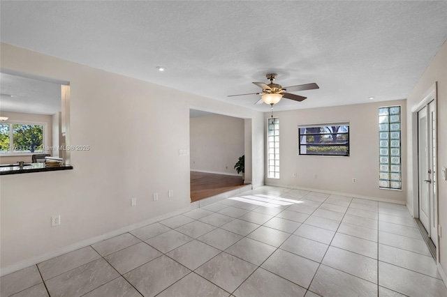 tiled spare room featuring baseboards, a textured ceiling, and a ceiling fan