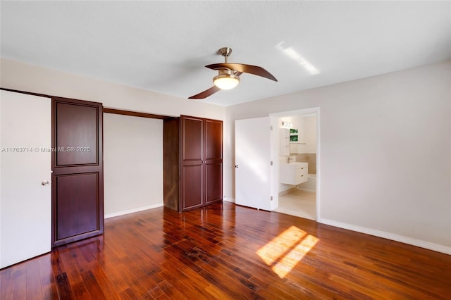 unfurnished bedroom featuring a ceiling fan, dark wood-style floors, baseboards, and ensuite bathroom