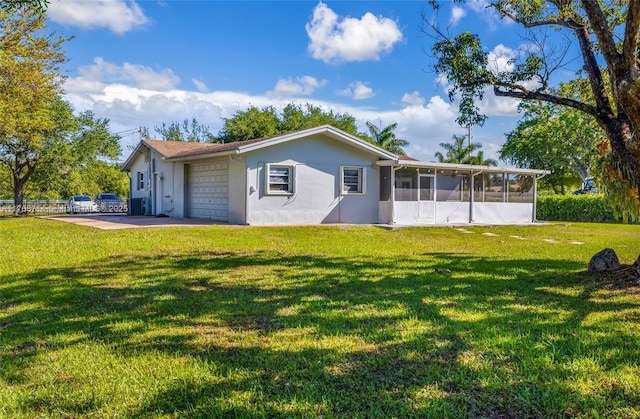 back of property featuring stucco siding, a lawn, an attached garage, and a sunroom