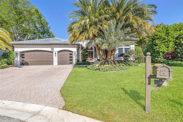 mediterranean / spanish-style home with a front yard, stucco siding, a garage, a tiled roof, and decorative driveway