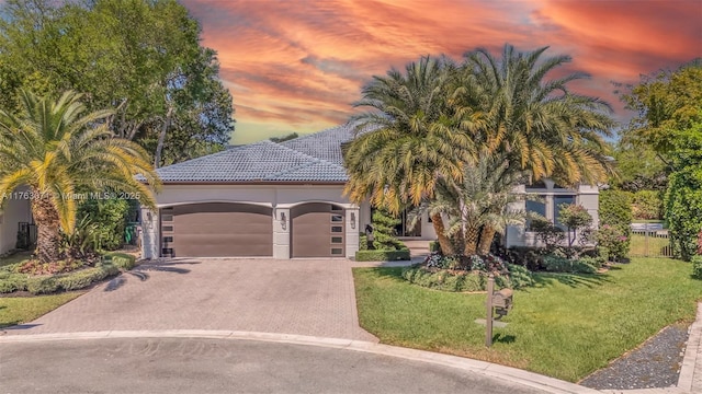 view of front facade featuring stucco siding, driveway, a yard, a garage, and a tiled roof