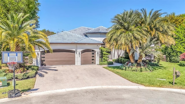 view of front of house featuring a front lawn, a tiled roof, stucco siding, driveway, and an attached garage