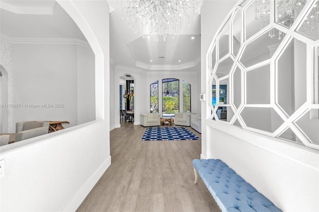 foyer with a tray ceiling, arched walkways, wood finished floors, and ornamental molding