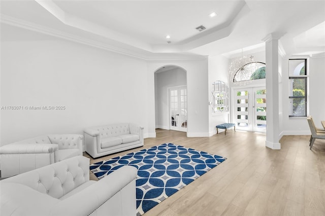 living room featuring wood finished floors, baseboards, visible vents, a tray ceiling, and arched walkways