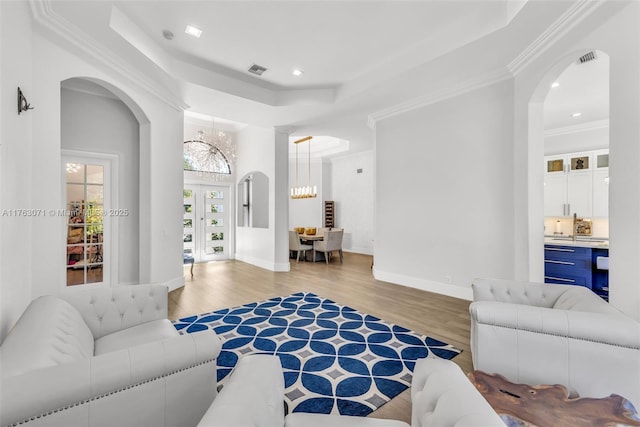 living area with visible vents, a chandelier, light wood-style floors, arched walkways, and a raised ceiling