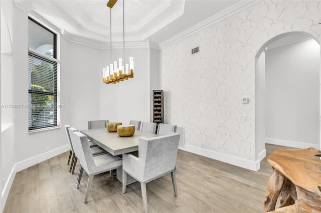 dining space featuring baseboards, a tray ceiling, ornamental molding, light wood-style flooring, and arched walkways