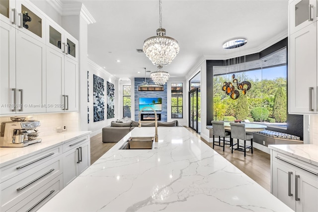 kitchen with open floor plan, white cabinetry, an inviting chandelier, crown molding, and decorative backsplash