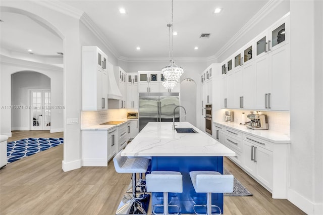 kitchen with visible vents, a kitchen island with sink, arched walkways, a sink, and appliances with stainless steel finishes