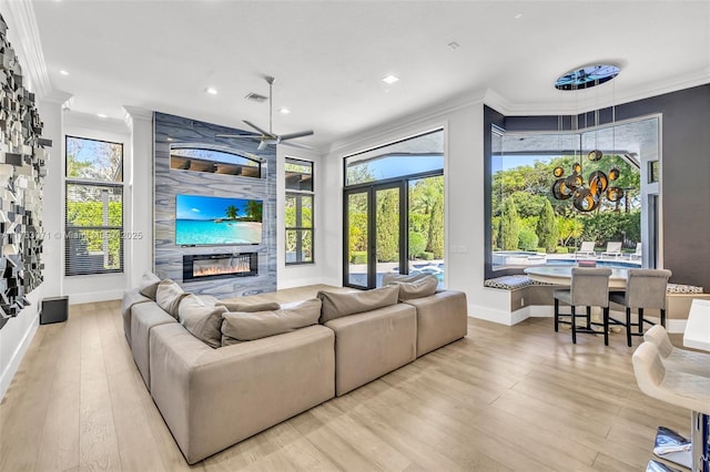 living area featuring ceiling fan, a large fireplace, light wood-style floors, and ornamental molding