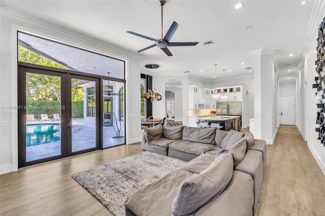 living area featuring visible vents, light wood-type flooring, ceiling fan, and ornamental molding