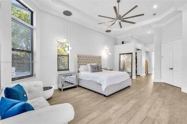 bedroom featuring baseboards, a tray ceiling, ornamental molding, a towering ceiling, and light wood-type flooring