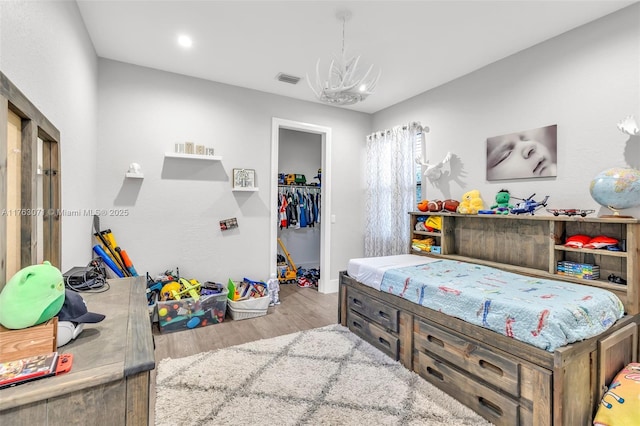 bedroom featuring a spacious closet, visible vents, a chandelier, wood finished floors, and a closet