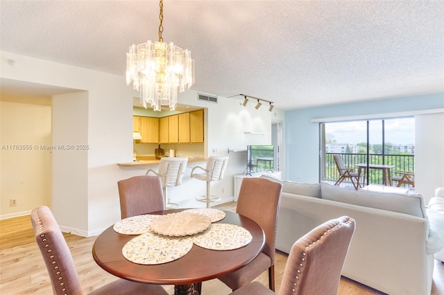 dining space with a chandelier, visible vents, a textured ceiling, and light wood-style floors