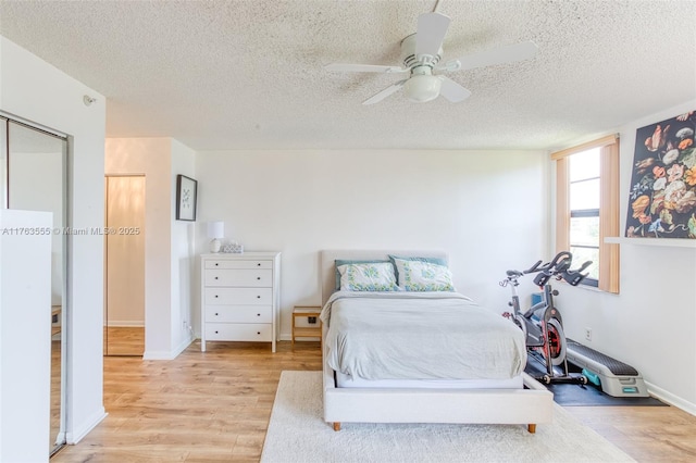 bedroom with a textured ceiling, a ceiling fan, freestanding refrigerator, and light wood-style floors