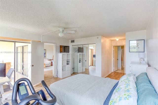 bedroom with visible vents, a textured ceiling, light wood-type flooring, and a ceiling fan