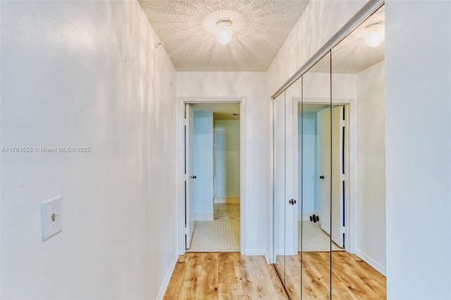 hallway featuring light wood-type flooring, baseboards, and a textured ceiling