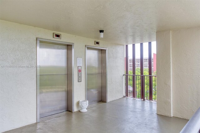 empty room featuring elevator, a textured ceiling, finished concrete floors, and a textured wall