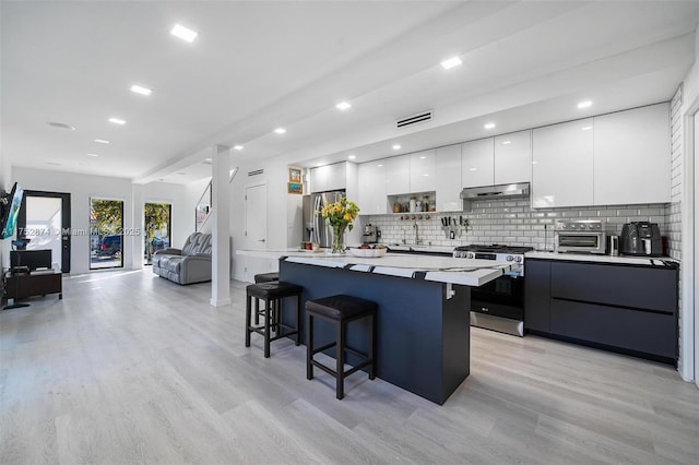 kitchen with a breakfast bar area, a kitchen island, stainless steel appliances, under cabinet range hood, and modern cabinets