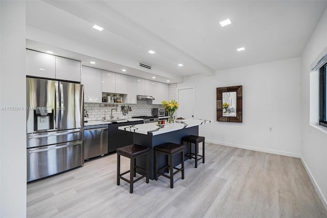 kitchen featuring a breakfast bar, stainless steel appliances, white cabinetry, modern cabinets, and backsplash