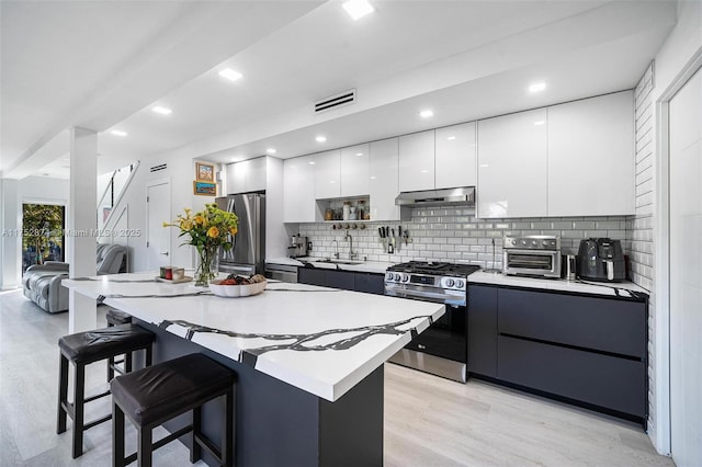 kitchen featuring modern cabinets, under cabinet range hood, a sink, stainless steel appliances, and a breakfast bar area