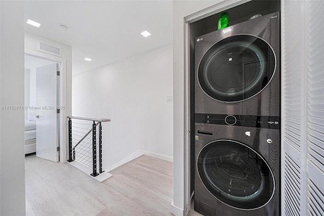 clothes washing area with visible vents, baseboards, laundry area, stacked washer and clothes dryer, and wood finished floors