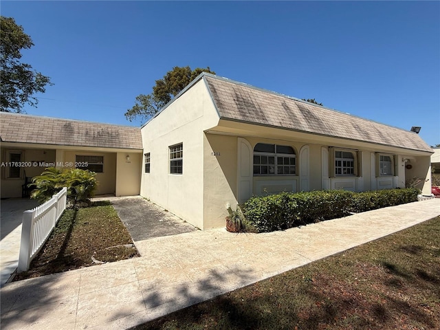 view of front facade with stucco siding, roof with shingles, and fence