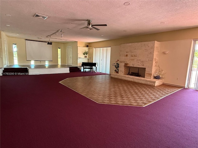 unfurnished living room featuring visible vents, a textured ceiling, carpet floors, a large fireplace, and ceiling fan