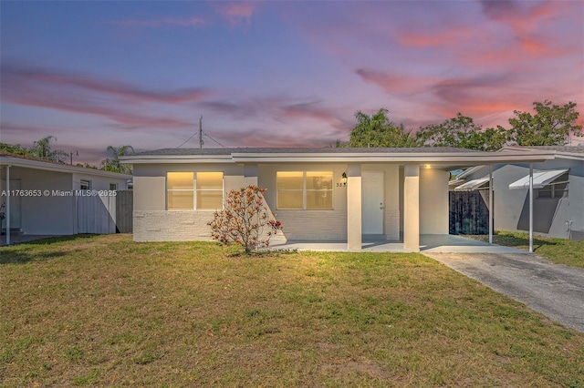 back of property at dusk featuring a yard, a carport, stucco siding, and aphalt driveway