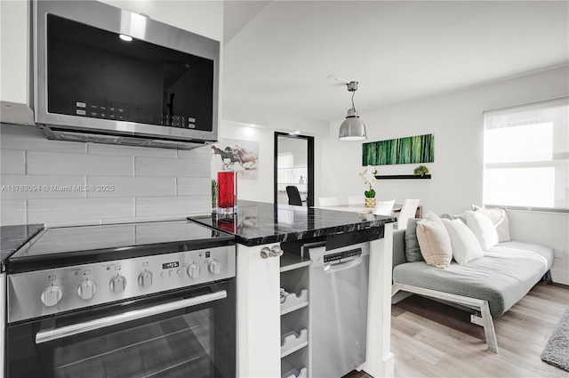 kitchen with dark countertops, appliances with stainless steel finishes, a peninsula, wood finished floors, and hanging light fixtures