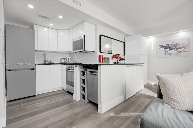 619 Euclid Ave Unit 1B, Miami Beach, FL 33139 - kitchen with appliances with stainless steel finishes, dark countertops, white cabinets, light wood-style flooring, and backsplash