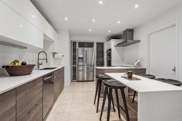 kitchen with a sink, stainless steel appliances, light countertops, wall chimney exhaust hood, and modern cabinets