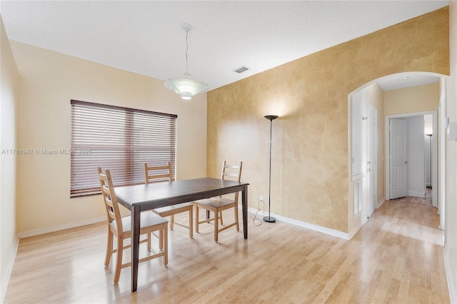 dining area with arched walkways, visible vents, baseboards, and light wood-style floors