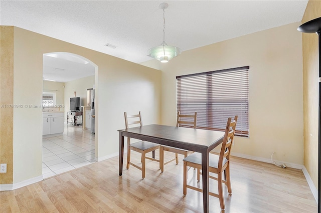 dining area featuring light wood finished floors, visible vents, baseboards, arched walkways, and a textured ceiling